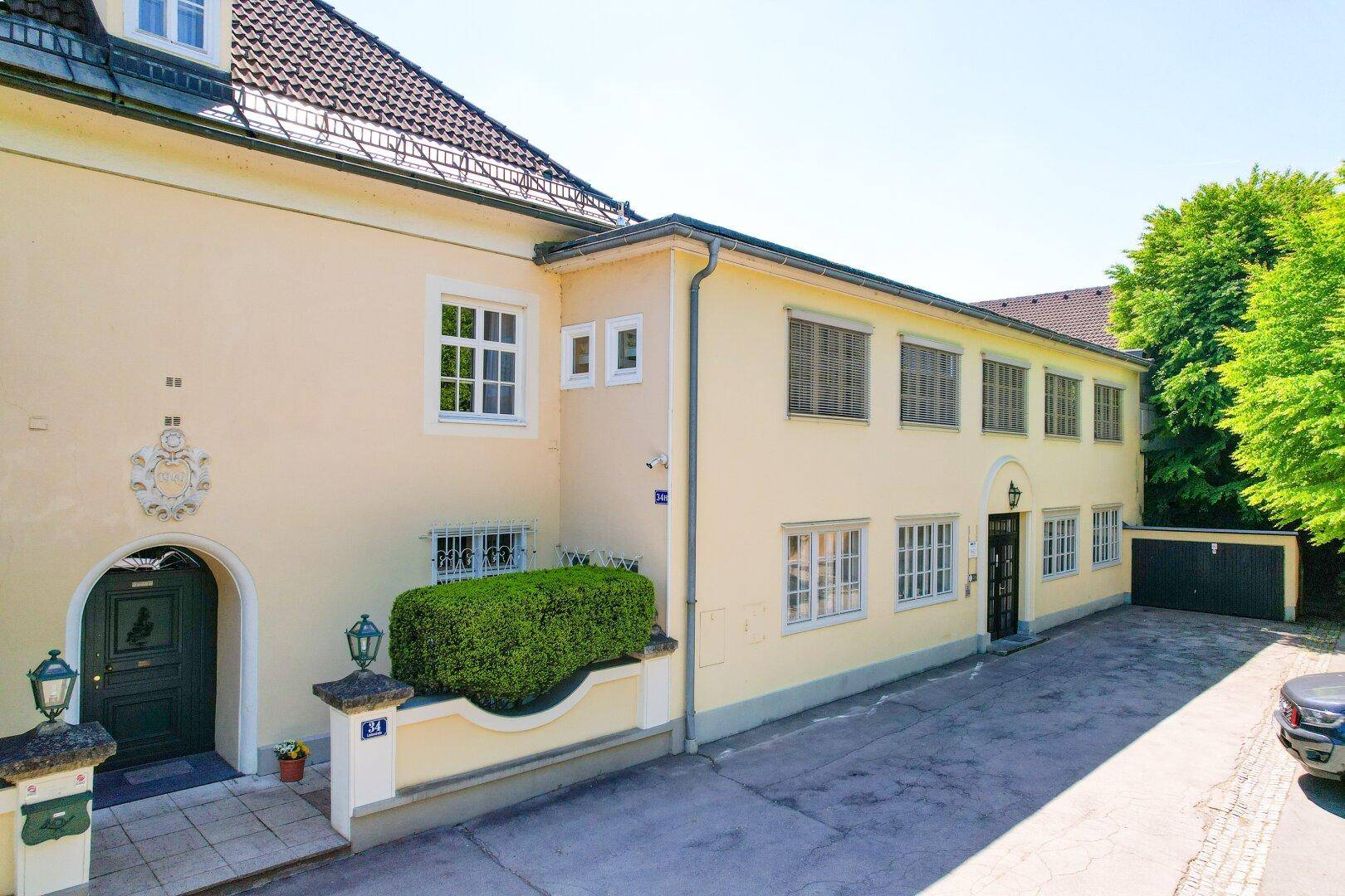 Historisches Gebäude mit gelber Fassade, grüner Eingangstür und gepflasterter Zufahrt.