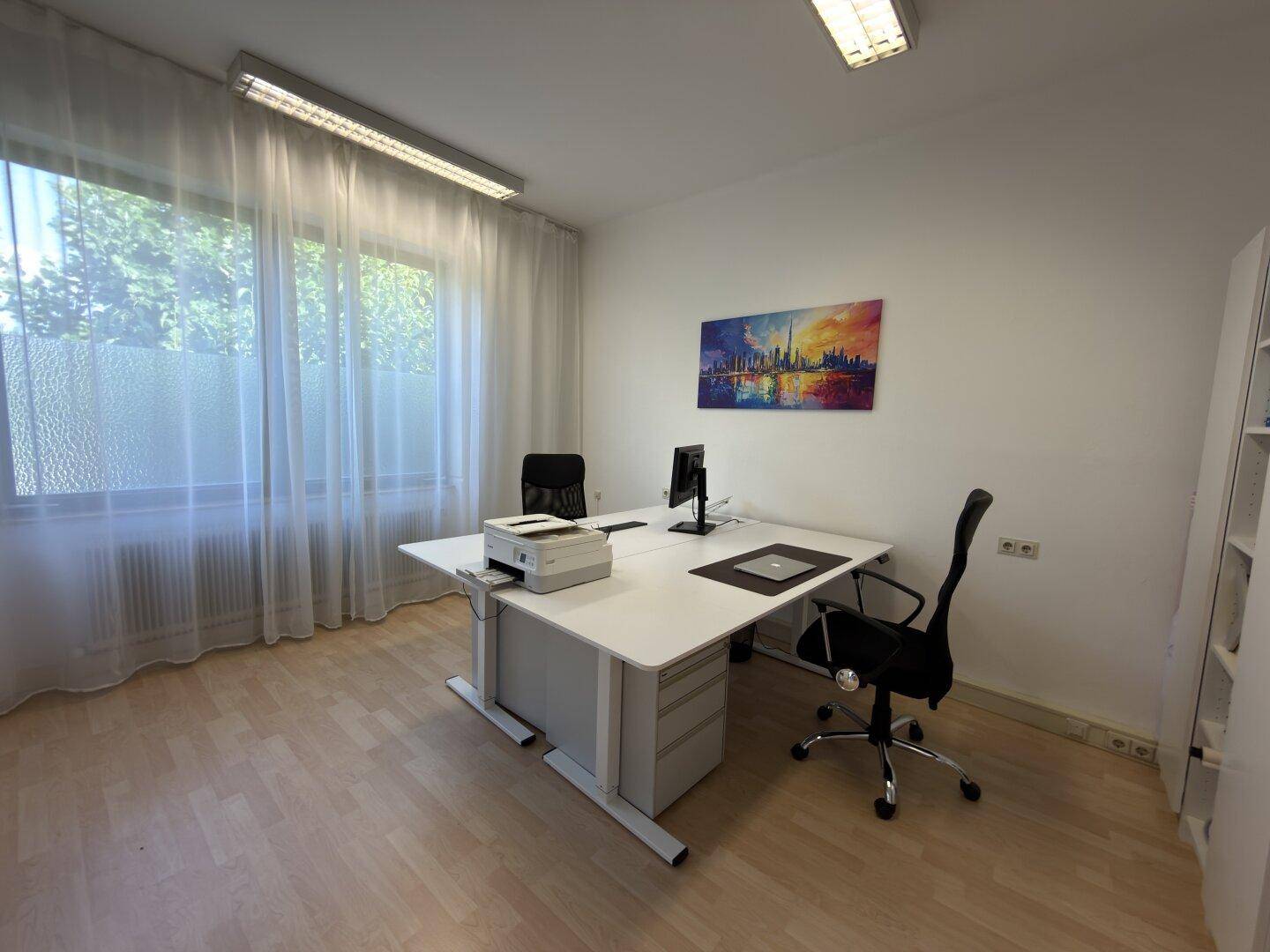 Helles Büro mit zwei Arbeitsplätzen, einem Fenster mit Vorhängen und einem farbenfrohen Wandbild.