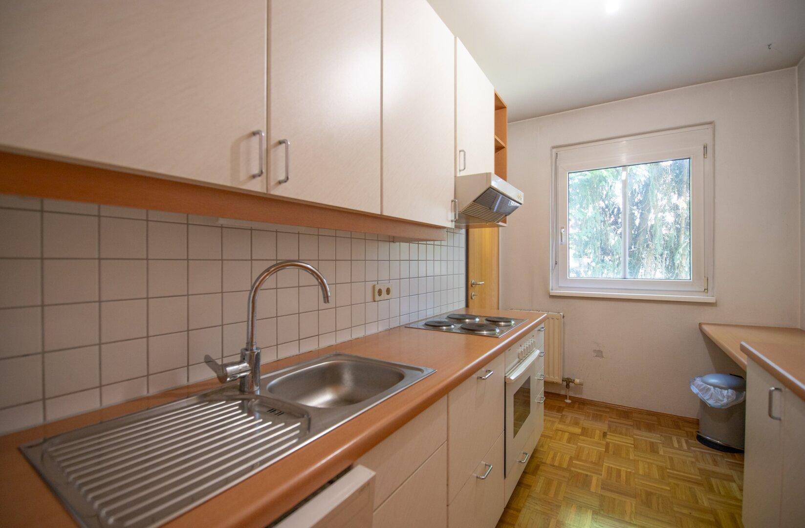 Funktionale Küche mit hellen Schränken, Fliesenrückwand und einem Fenster mit Blick ins Grüne.