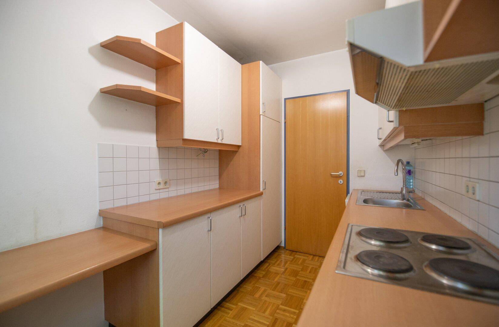 Einfache Küche mit hellen Schränken, Holztheke und Fliesenrückwand, bereit zur Nutzung.