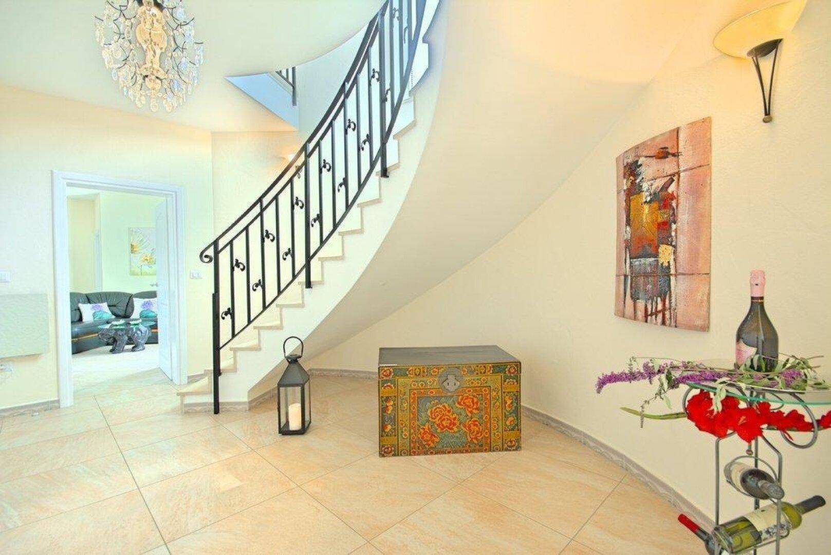 Eleganter Flur mit geschwungener Treppe, Fliesenboden und dekorativen Elementen.