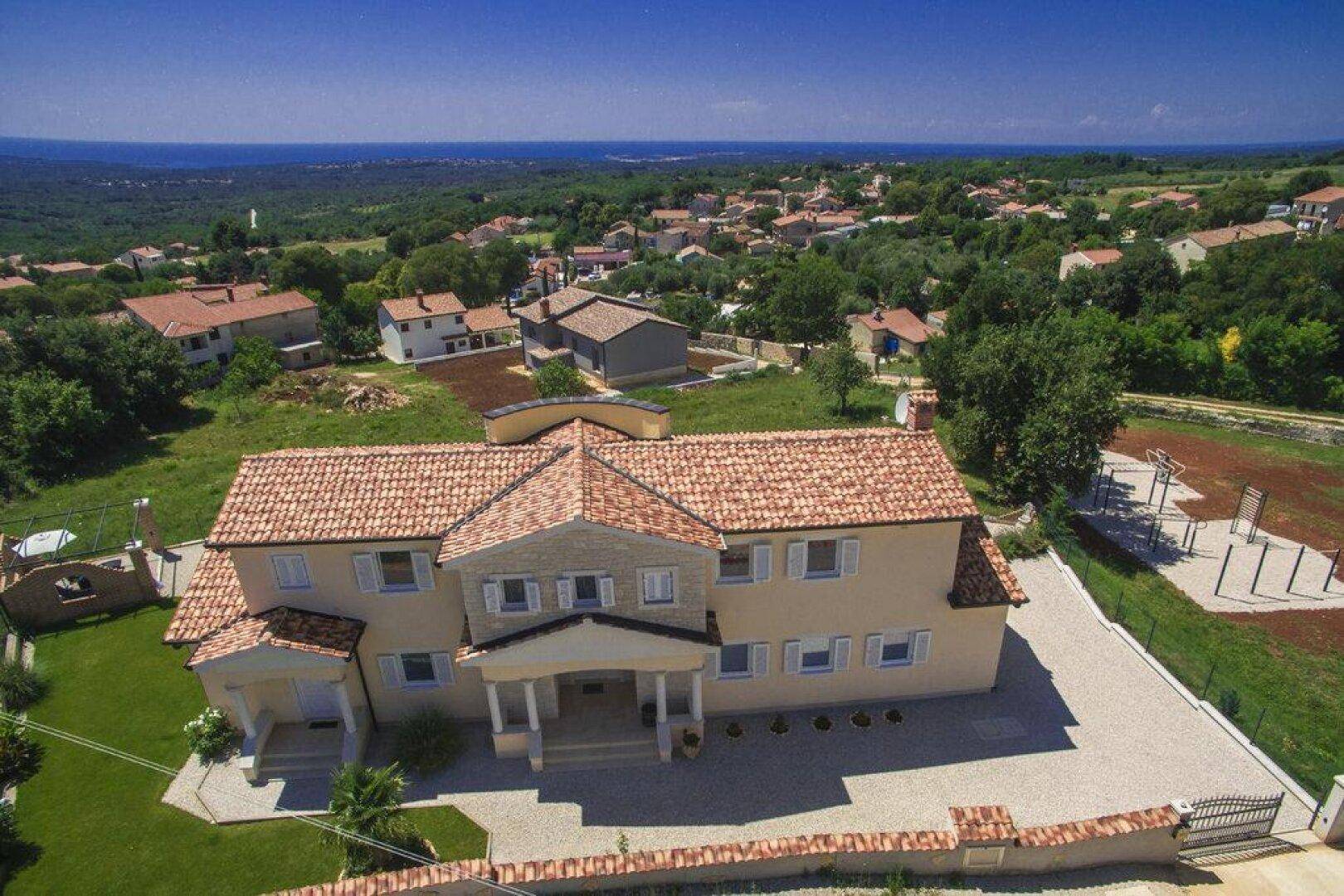 Luftaufnahme der Villa mit rotem Ziegeldach, umgeben von grüner Landschaft und Meerblick in der Ferne.