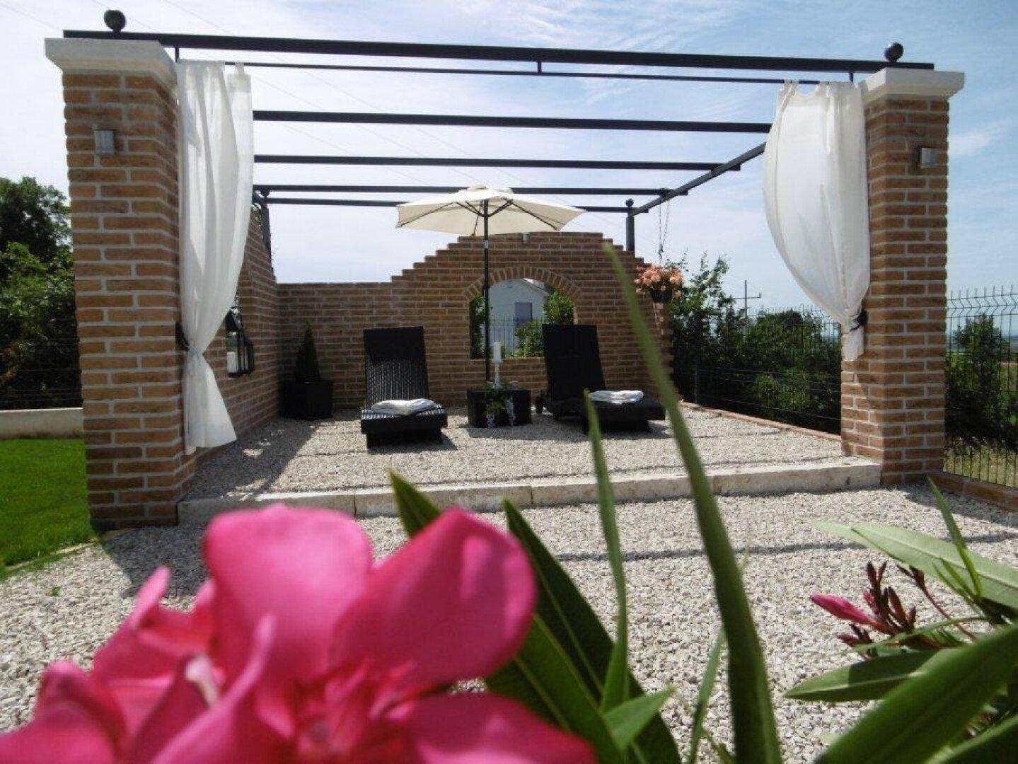 Entspannungsbereich im Freien mit Pergola, Sonnenliegen und dekorativer Ziegelwand.