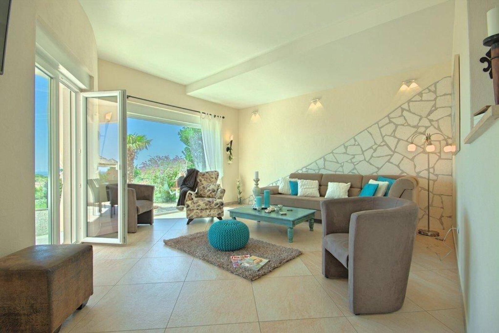 Helles Wohnzimmer mit beigefarbenen Fliesen, gemütlicher Couch und Zugang zur Terrasse.