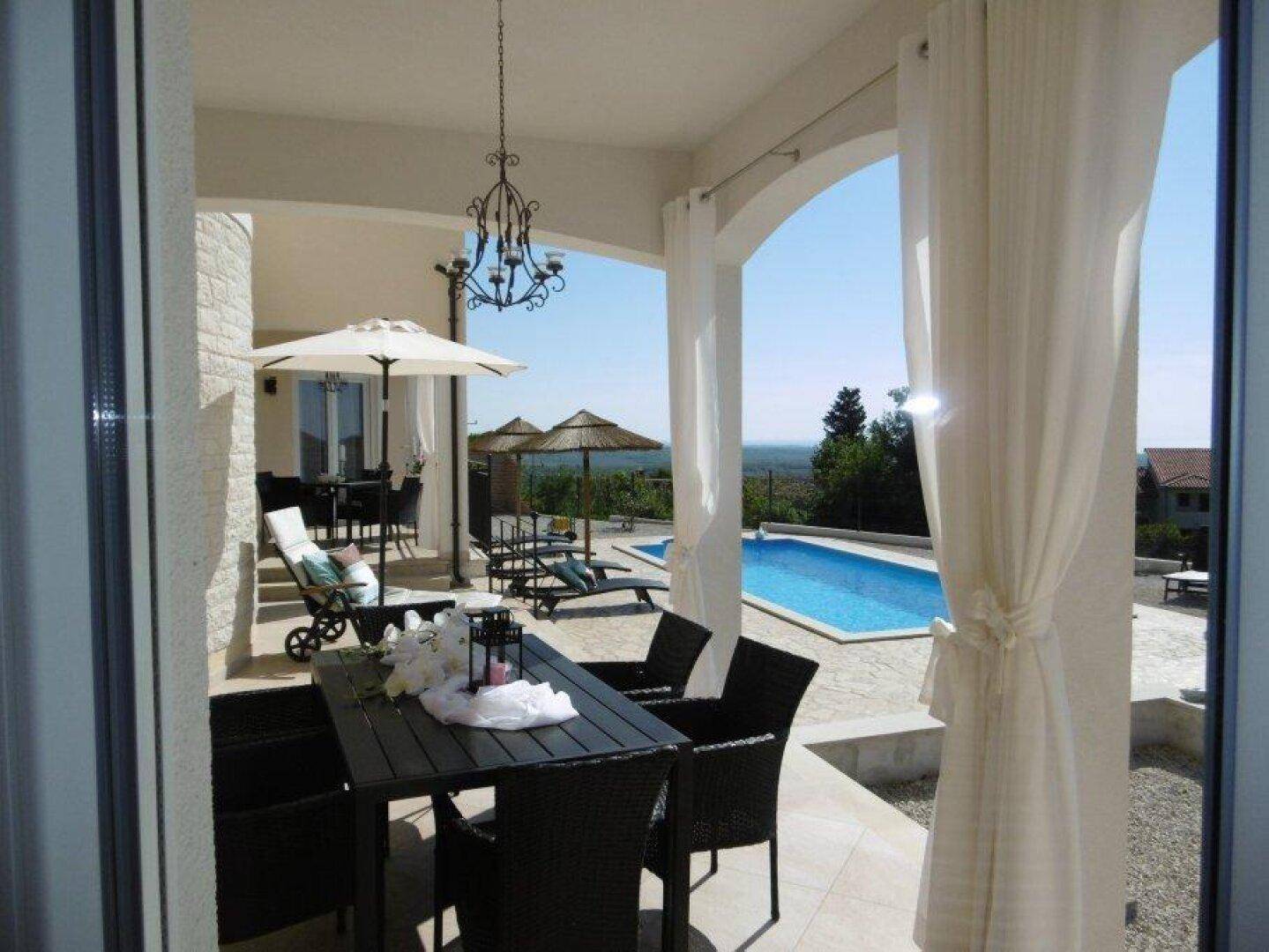 Überdachte Terrasse mit Esstisch und Stühlen, ideal für Mahlzeiten im Freien mit Poolblick.
