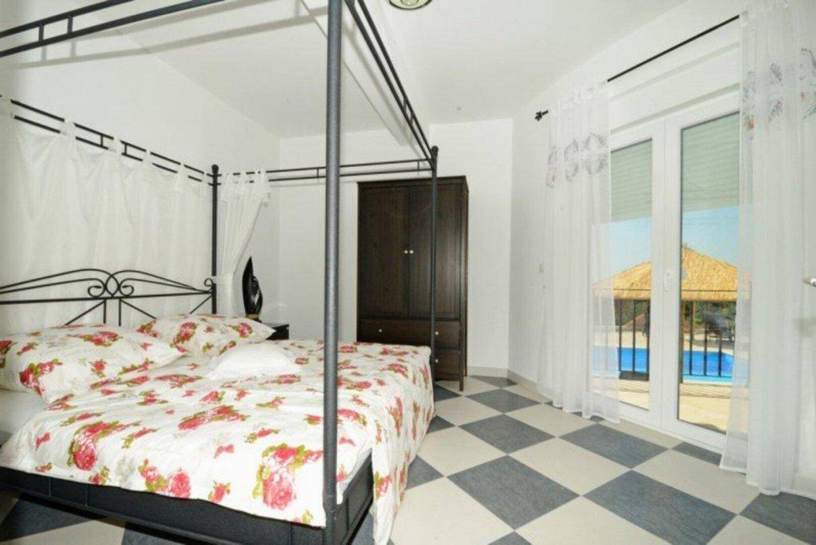 Schlafzimmer mit Himmelbett, kariertem Fliesenboden und Zugang zu einem Balkon mit Poolblick.