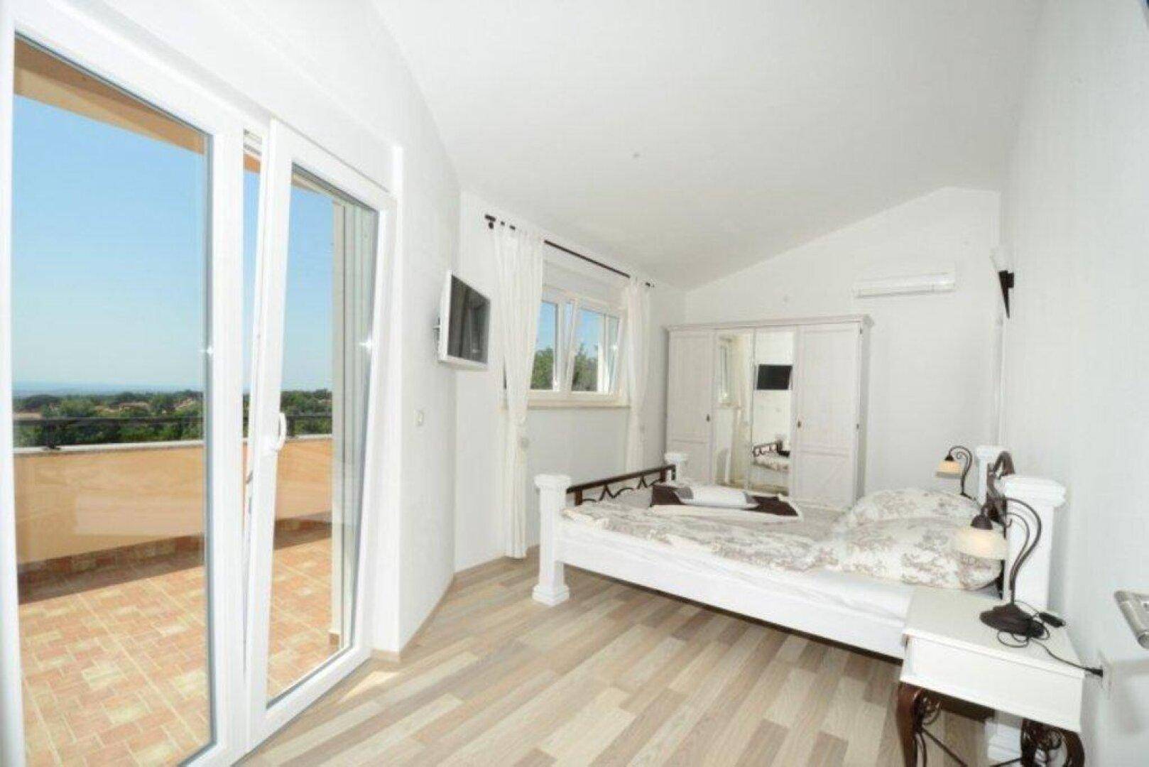 Helles Schlafzimmer mit Holzboden, weißem Bett und direktem Zugang zum Balkon.