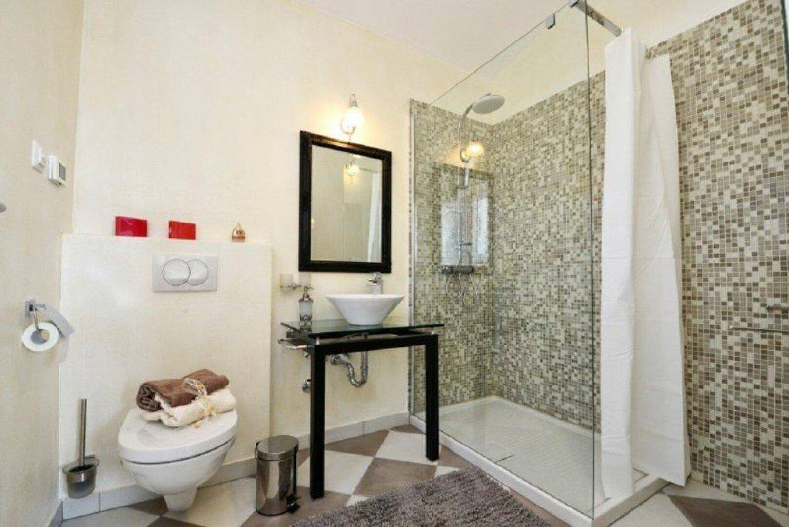 Modernes Badezimmer mit begehbarer Dusche, Mosaikfliesen und wandhängendem WC.