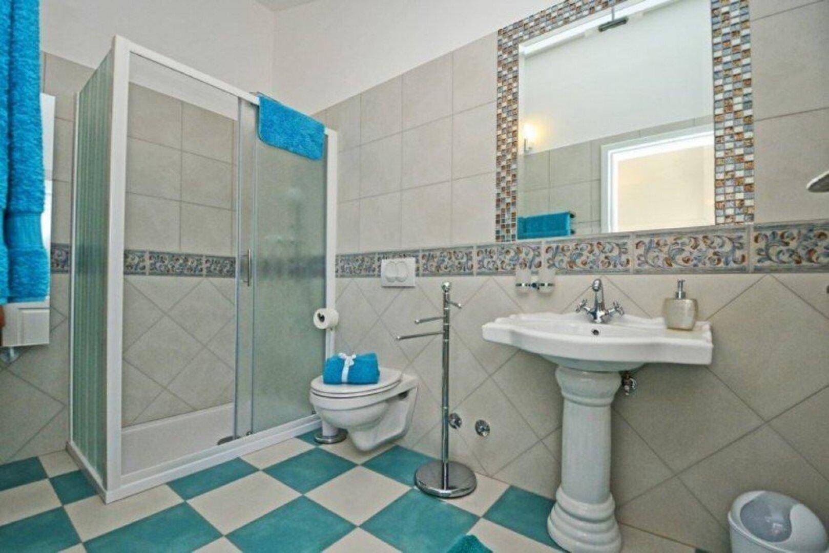 Badezimmer mit Duschkabine, Standwaschbecken und auffälligem blau-weiß kariertem Fliesenboden.