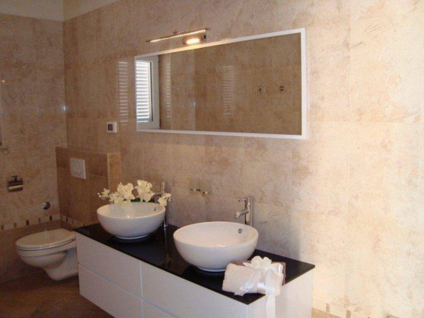 Elegantes Badezimmer mit Doppelwaschbecken, großem Spiegel und beigefarbenen Fliesen.