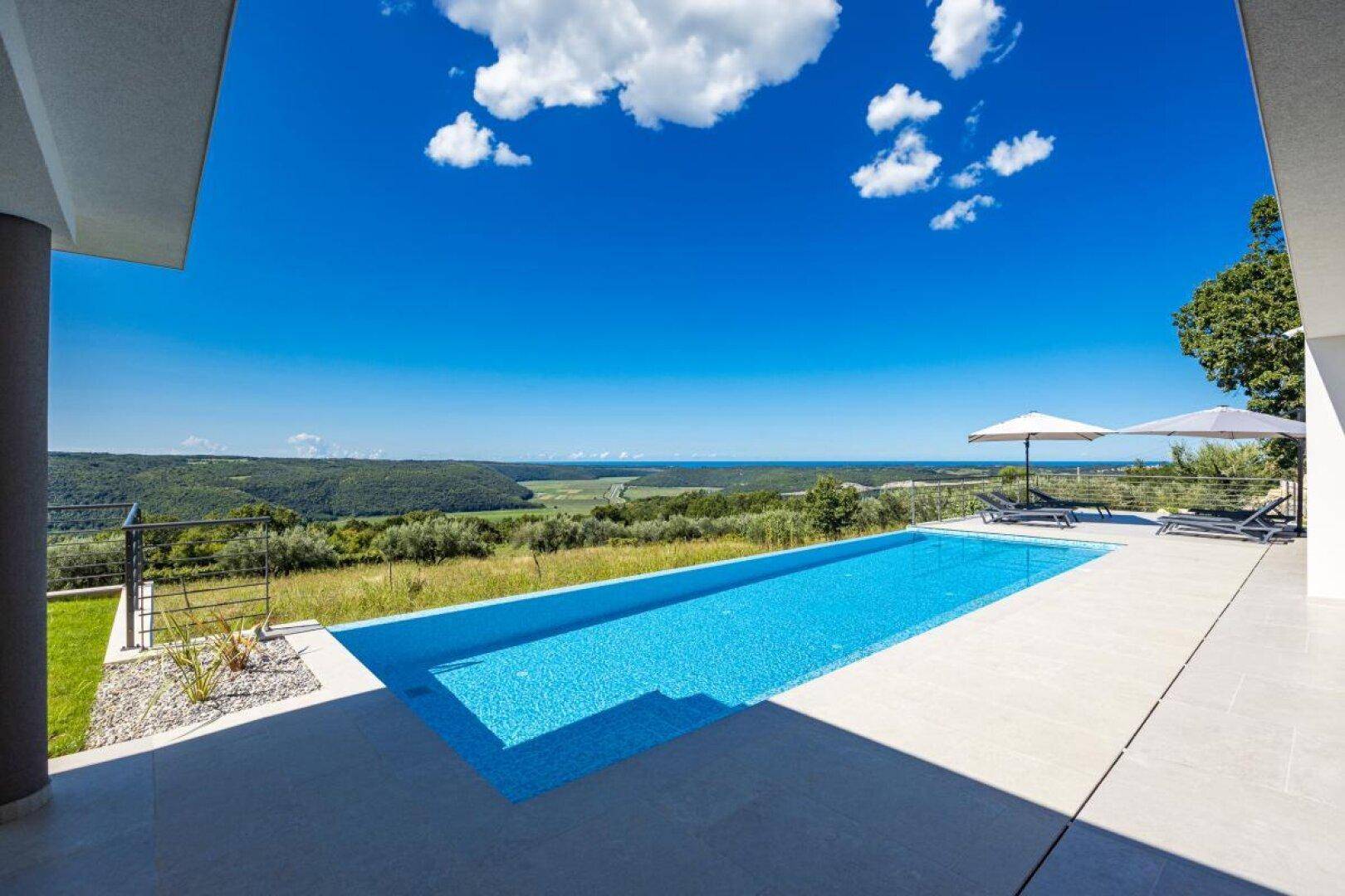 Langer, schmaler Pool mit Liegeflächen und weitem Blick auf die grüne Hügellandschaft.