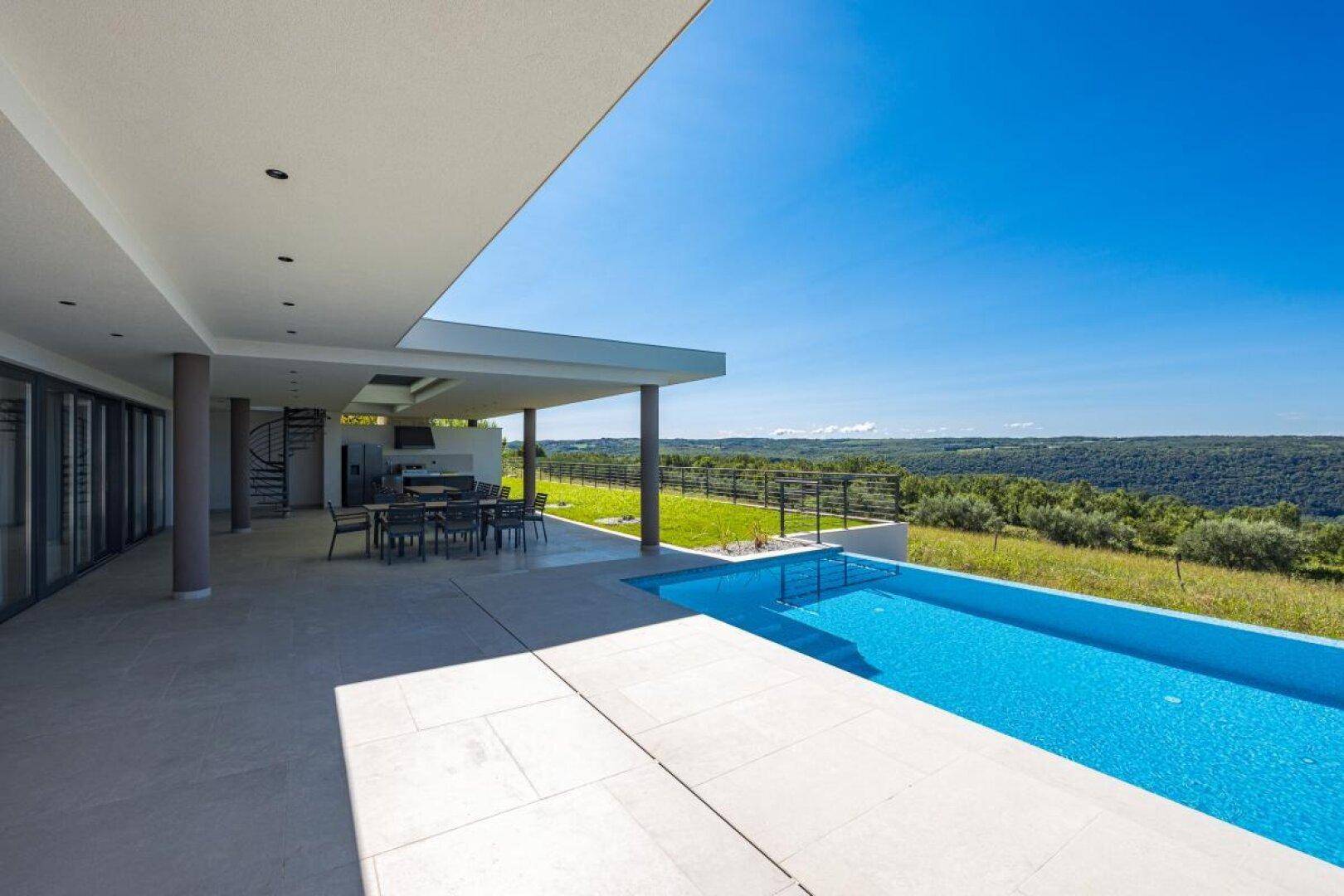 Überdachte Terrasse mit Essbereich und direktem Zugang zum Pool mit Landschaftsblick.