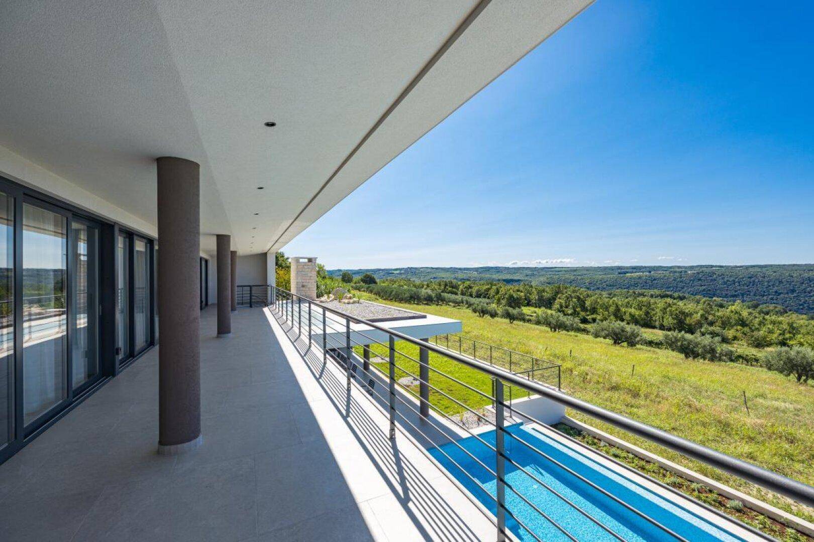 Langer Balkon mit Säulen und weitem Blick über den Pool und die grüne Landschaft.