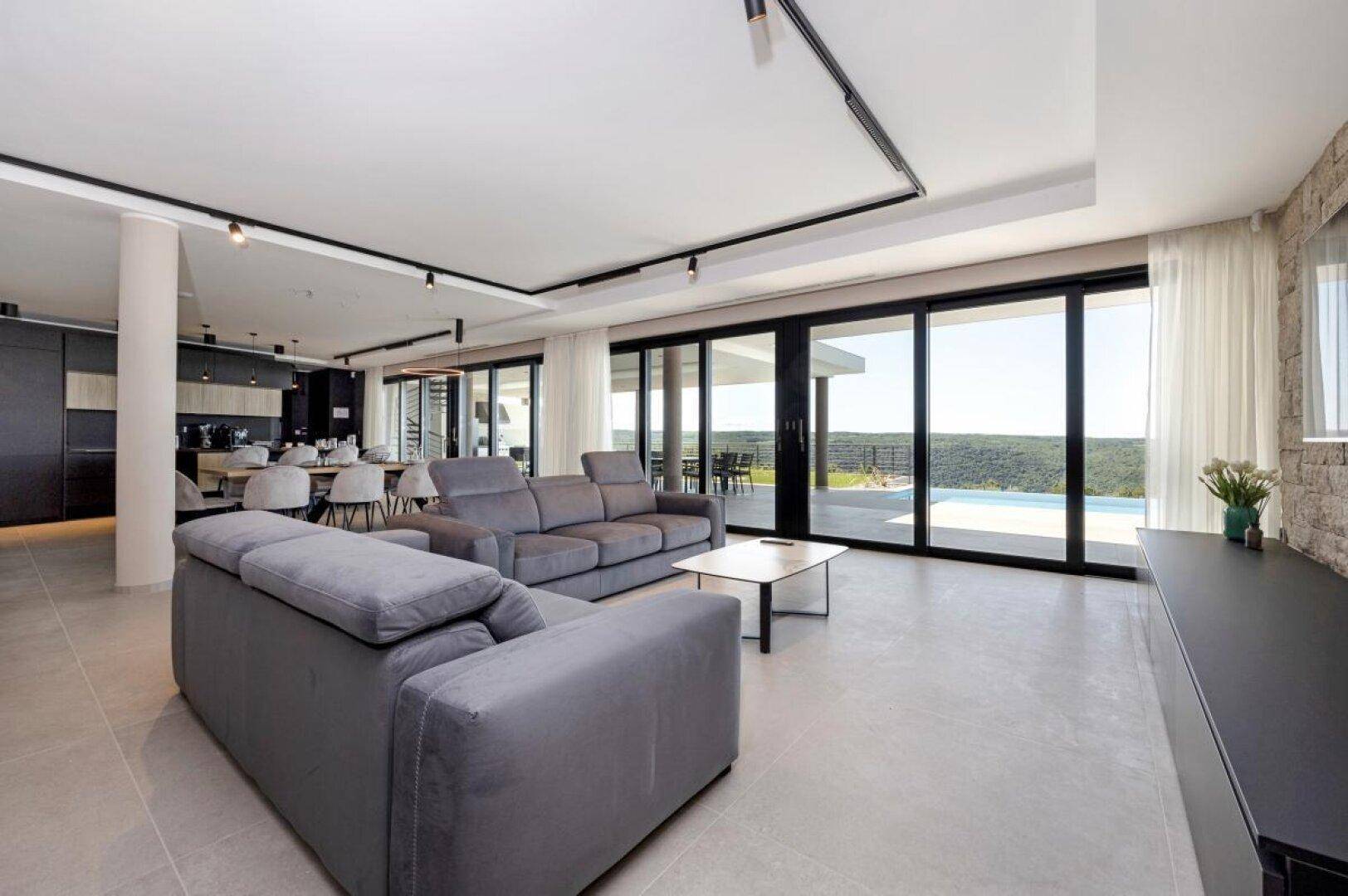 Modernes Wohnzimmer mit bequemen Sofas, großen Fenstern und Panoramablick ins Grüne.