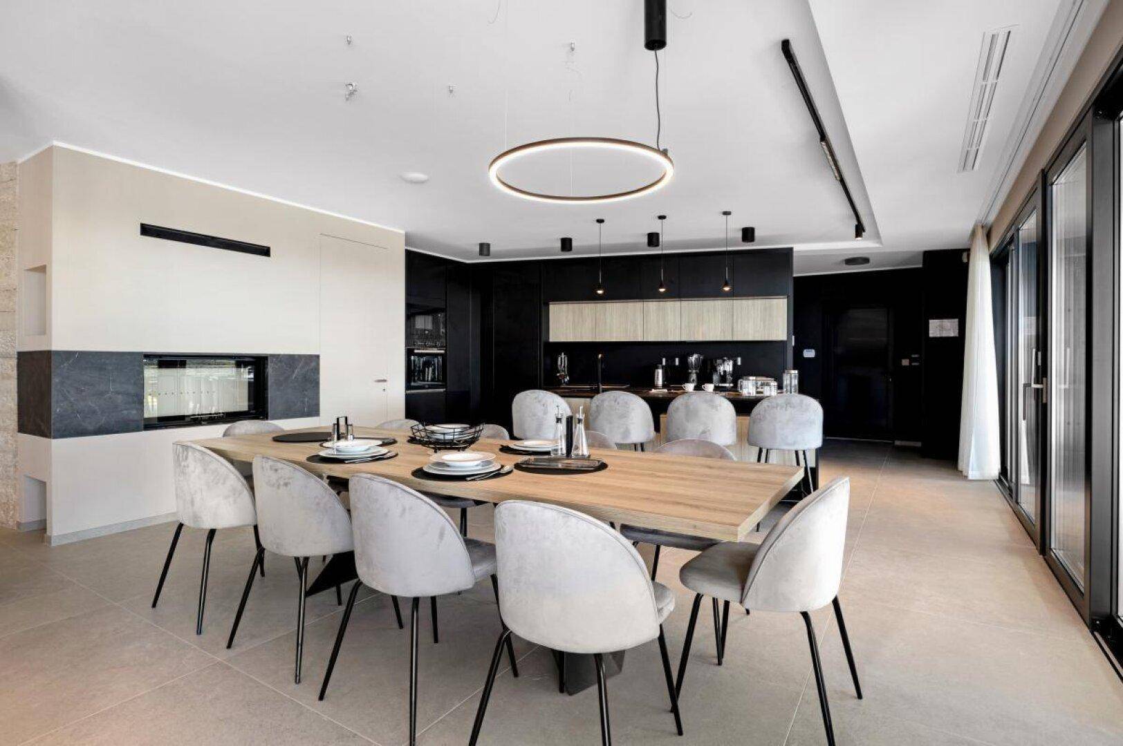 Eleganter Essbereich mit großem Holztisch und moderner offener Küche mit Kamin.
