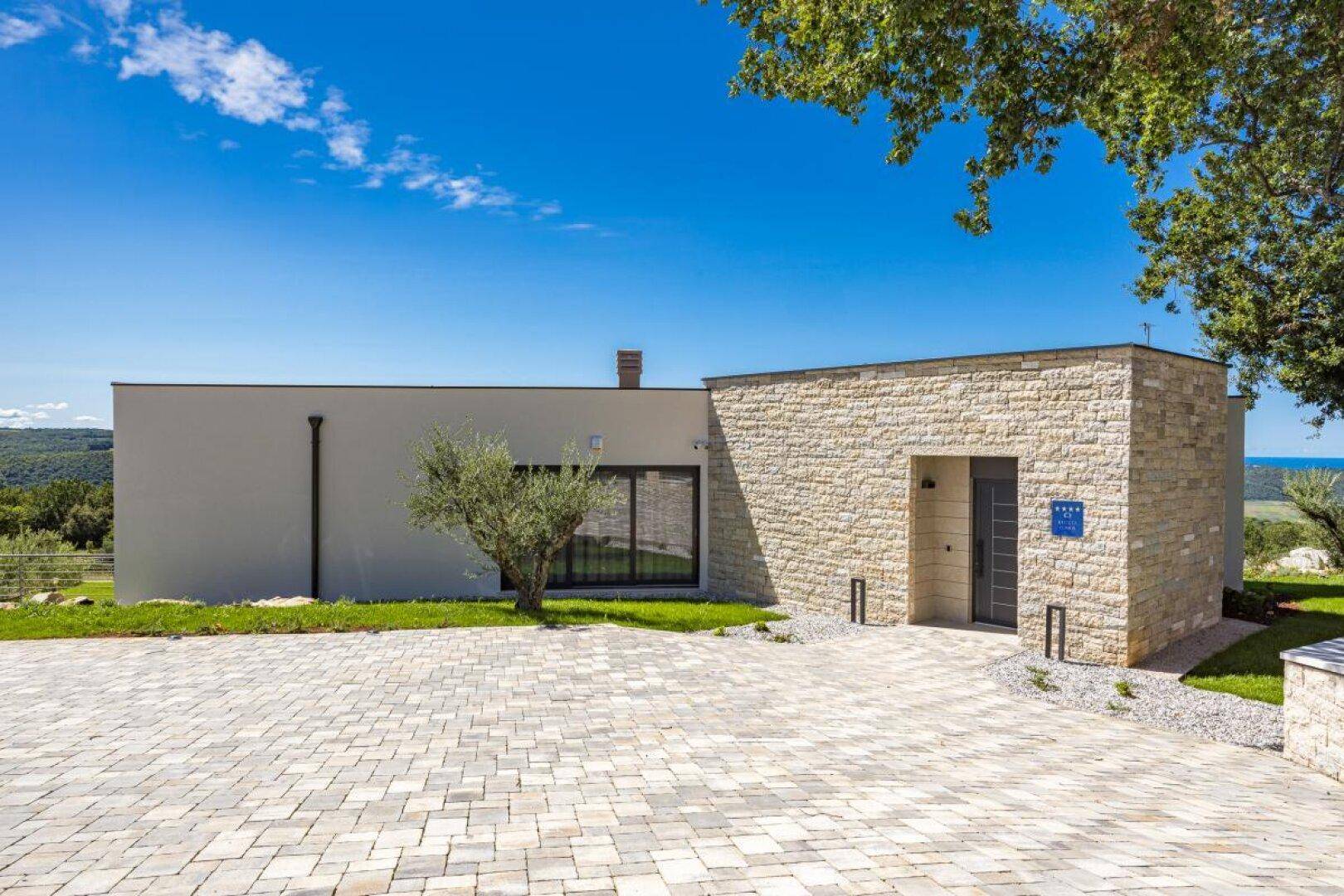 Moderne Villa mit Steinfassade, gepflasterter Auffahrt und mediterraner Bepflanzung.