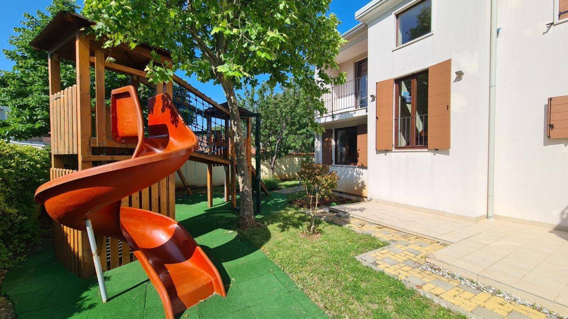 Kinderspielplatz mit Rutsche und Klettergerüst im grünen Garten neben dem Wohnhaus.