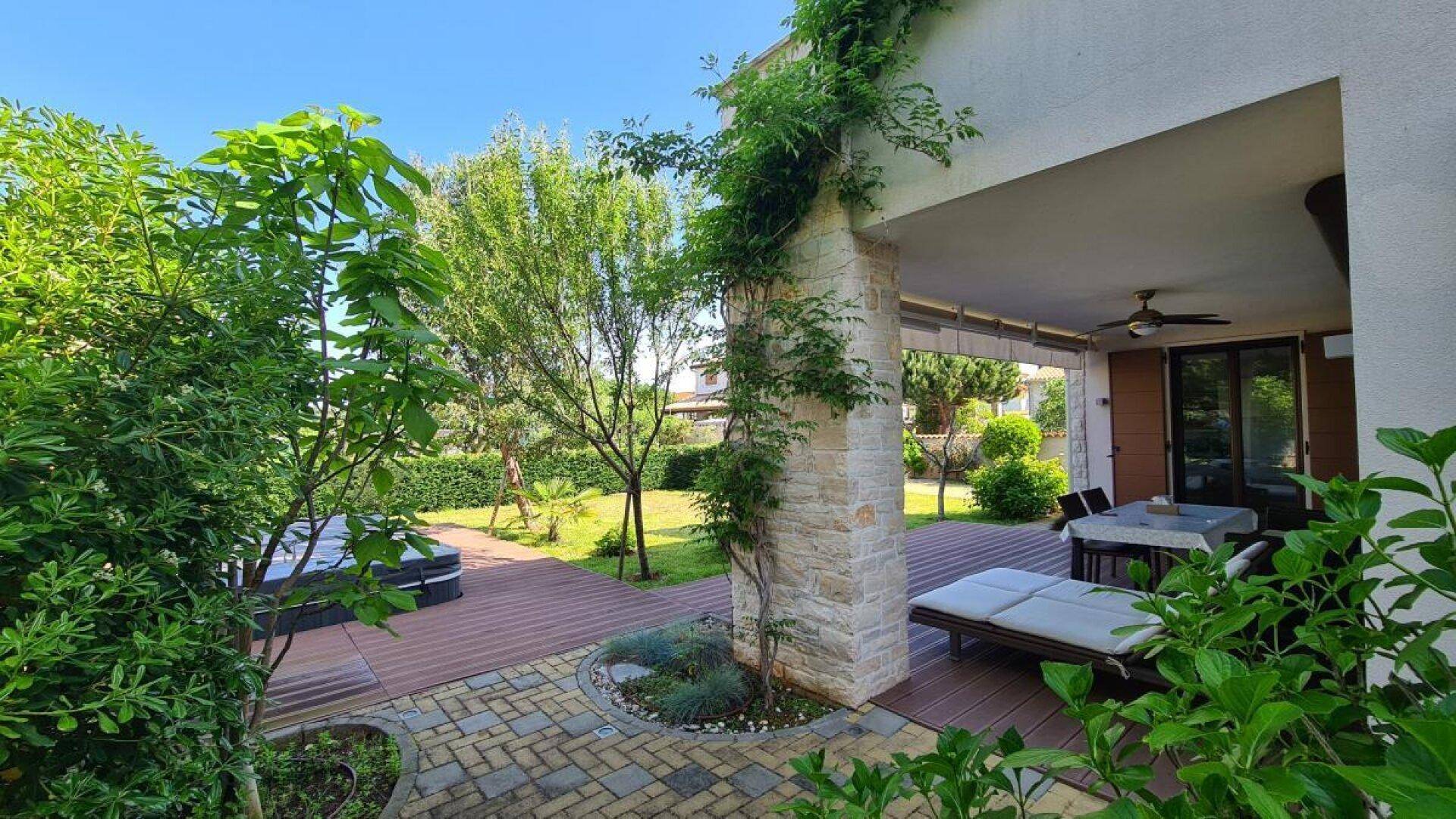 Überdachte Terrasse mit Holzdeck und Gartenmöbeln, umgeben von üppigem Grün für entspannte Stunden.