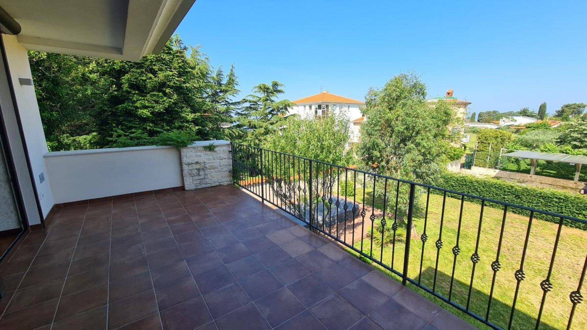 Geräumiger Balkon mit Fliesenboden und schmiedeeisernem Geländer, bietet Blick ins Grüne.