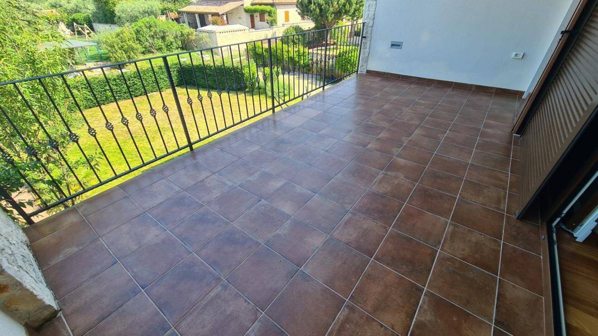 Großer Balkon mit braunen Fliesen und schwarzem Geländer, bietet weiten Blick auf die Umgebung.