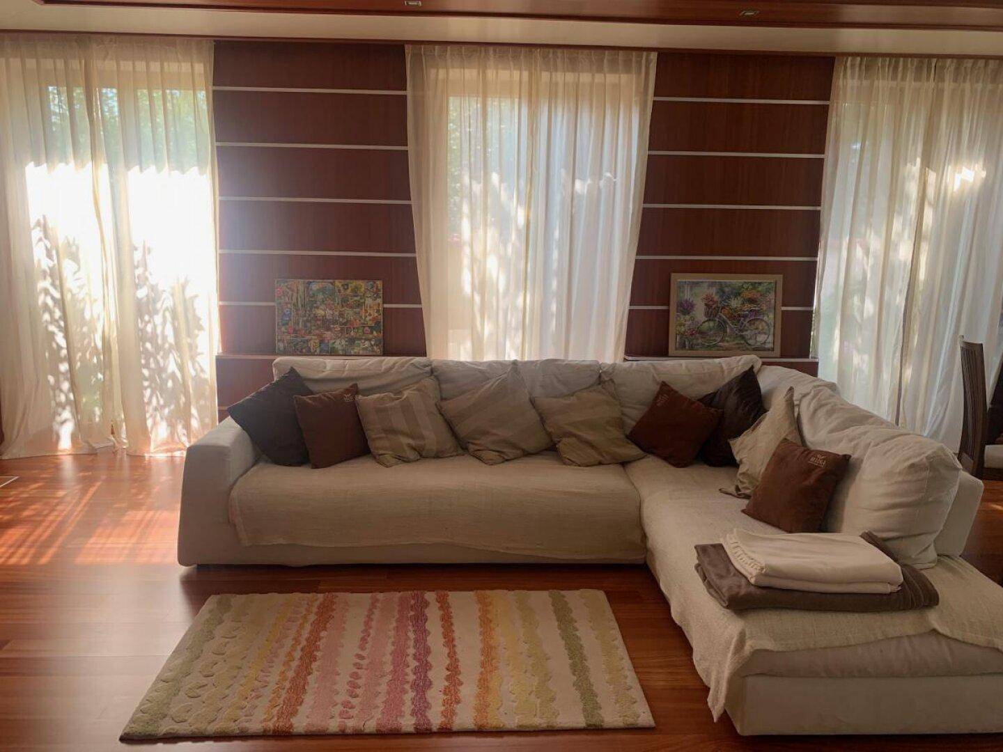 Lichtdurchflutetes Wohnzimmer mit großem Ecksofa, Holzboden und eleganten Vorhängen.