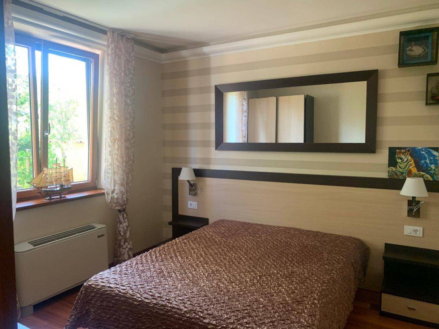 Helles Schlafzimmer mit Doppelbett, Holzboden und einem großen Spiegel über dem Bett.