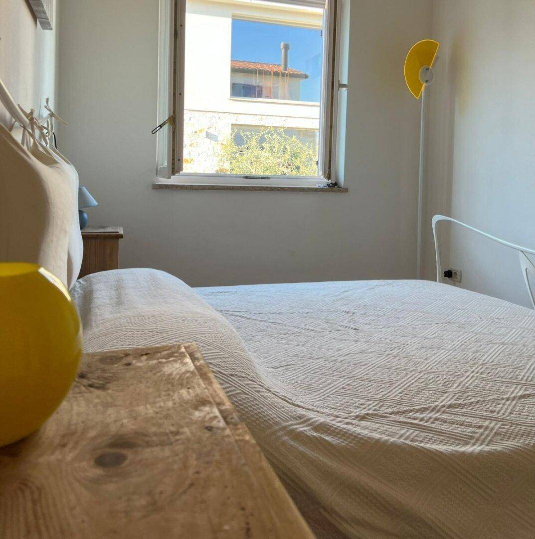 Helles Schlafzimmer mit weißem Bett und Fenster, das Tageslicht hereinlässt.