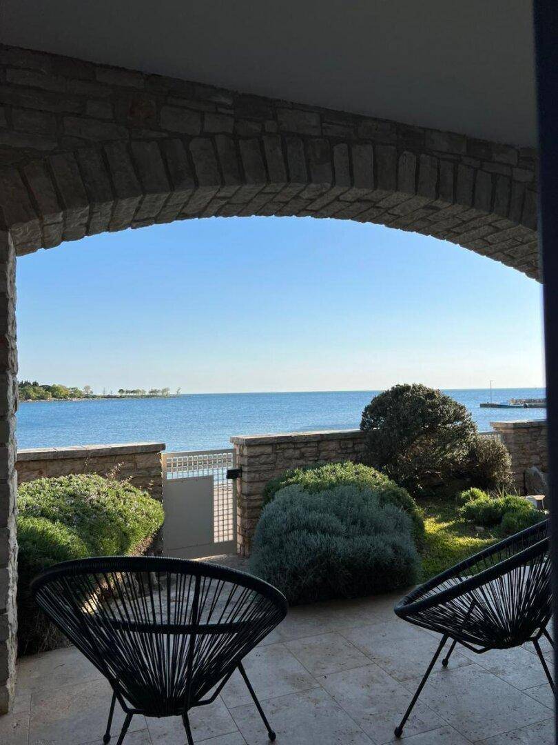 Überdachte Terrasse mit Steinbogen und bequemen Stühlen, bietet einen ruhigen Blick auf das Meer.