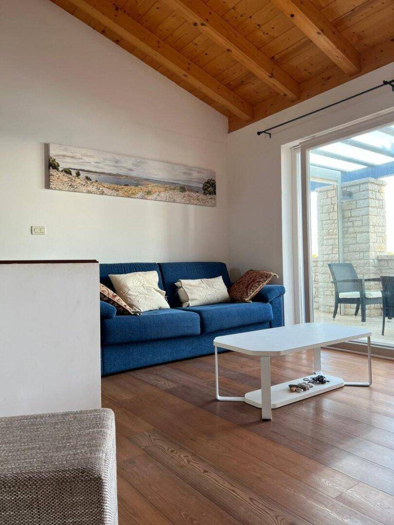 Wohnzimmer mit blauer Couch, Holzboden und Zugang zu einer sonnigen Terrasse.