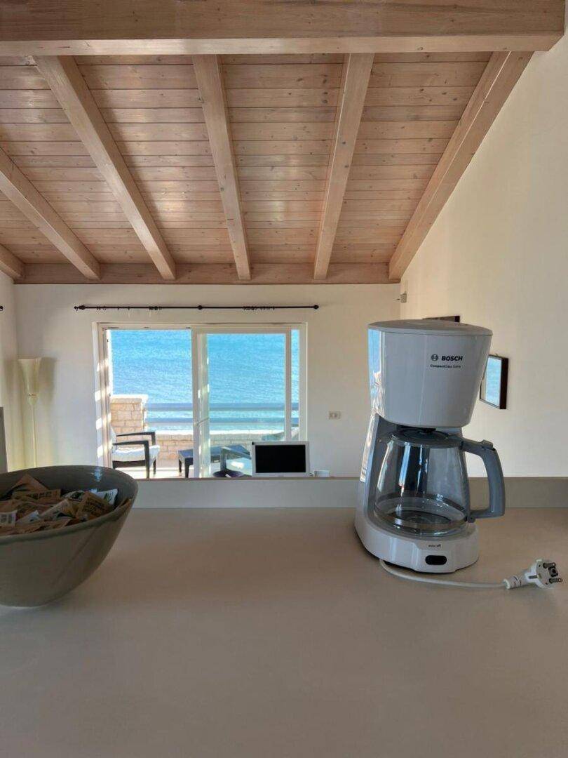 Küchenbereich mit Kaffeemaschine und Blick auf das Meer durch große Fenster.