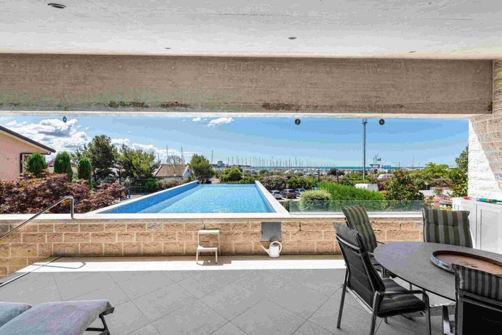 Überdachte Terrasse mit Esstisch, Liegestühlen und Blick auf den Infinity-Pool und das Meer.