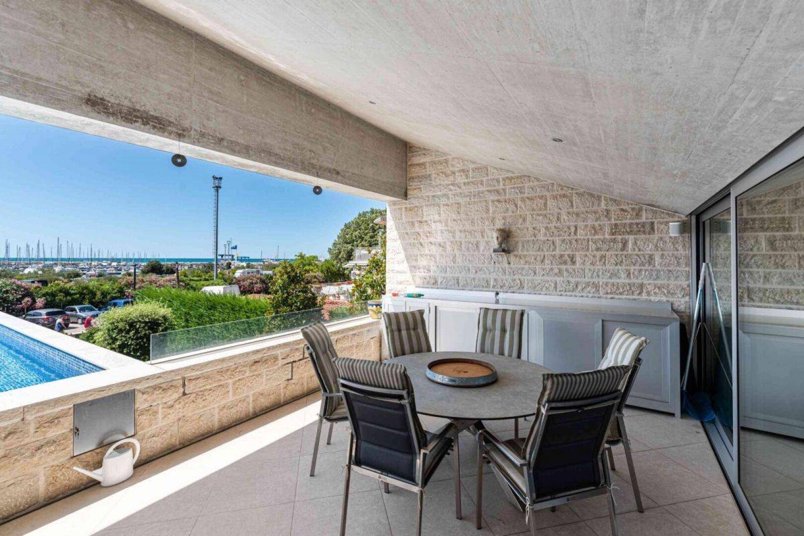 Geräumige Terrasse mit Esstisch und Stühlen, direkt am Pool mit Meerblick.