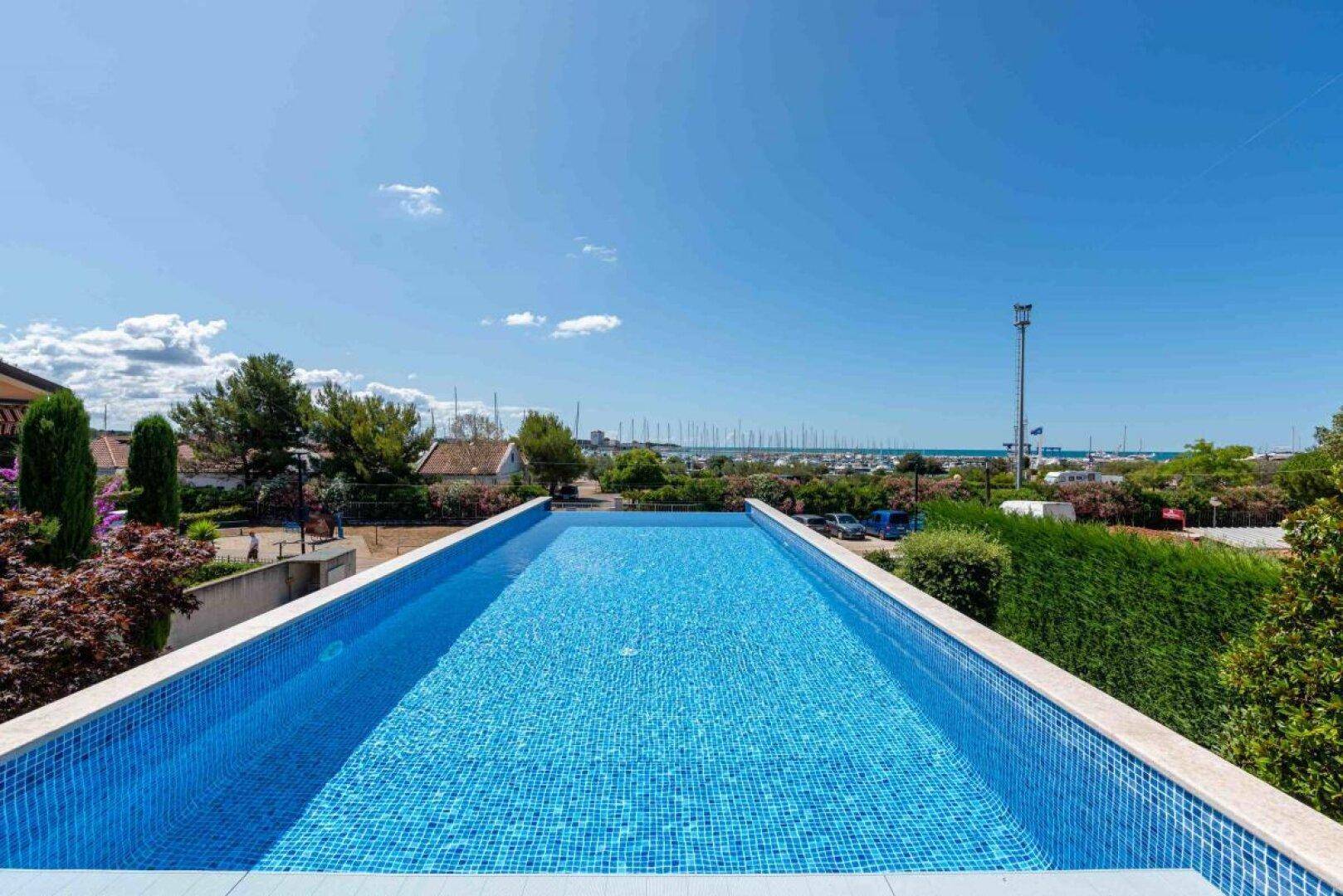 Langer, blauer Infinity-Pool mit Mosaikfliesen und weitem Blick auf das Meer und den Hafen.