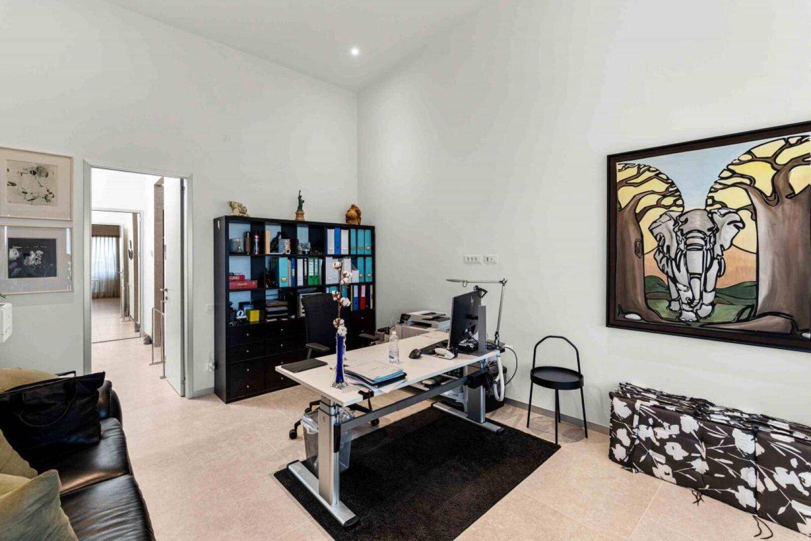 Helles Büro mit modernem Schreibtisch, Bücherregal und Kunstwerk an der Wand.