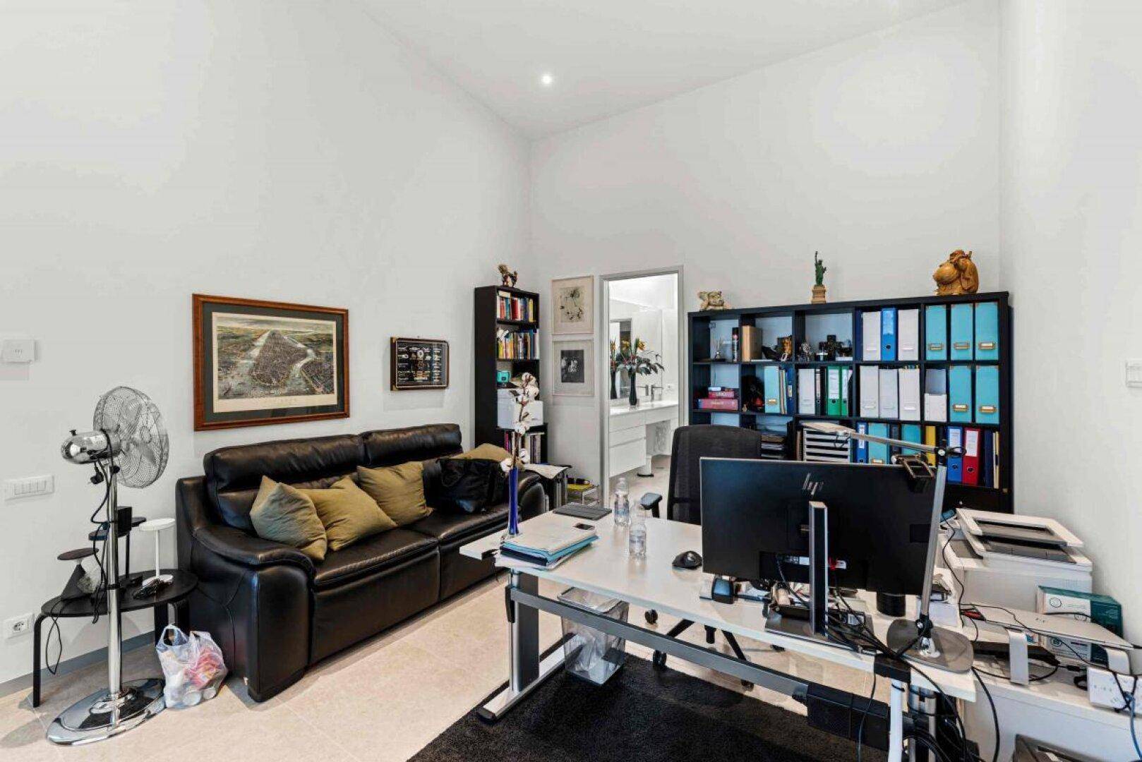 Geräumiges Büro mit Schreibtisch, Sofa und Blick in ein angrenzendes Badezimmer.