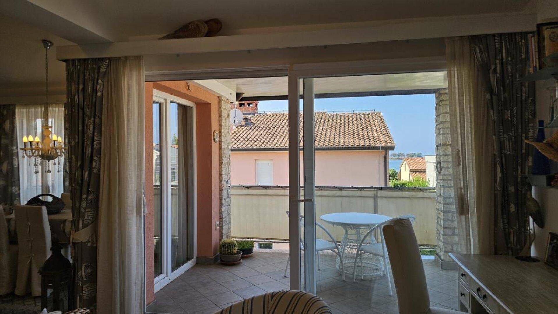 Blick vom Wohnbereich auf den möblierten Balkon mit Meerblick und umliegenden Gebäuden.