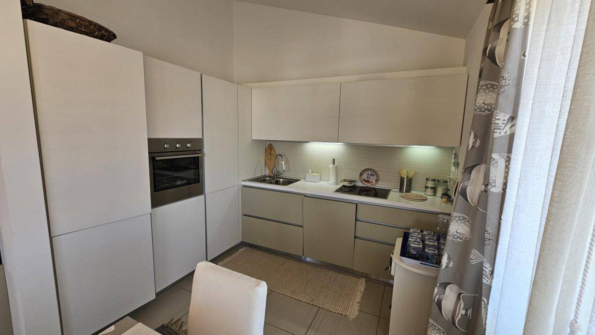 Moderne Küchenzeile mit hellen Schränken, integriertem Backofen und Induktionskochfeld.