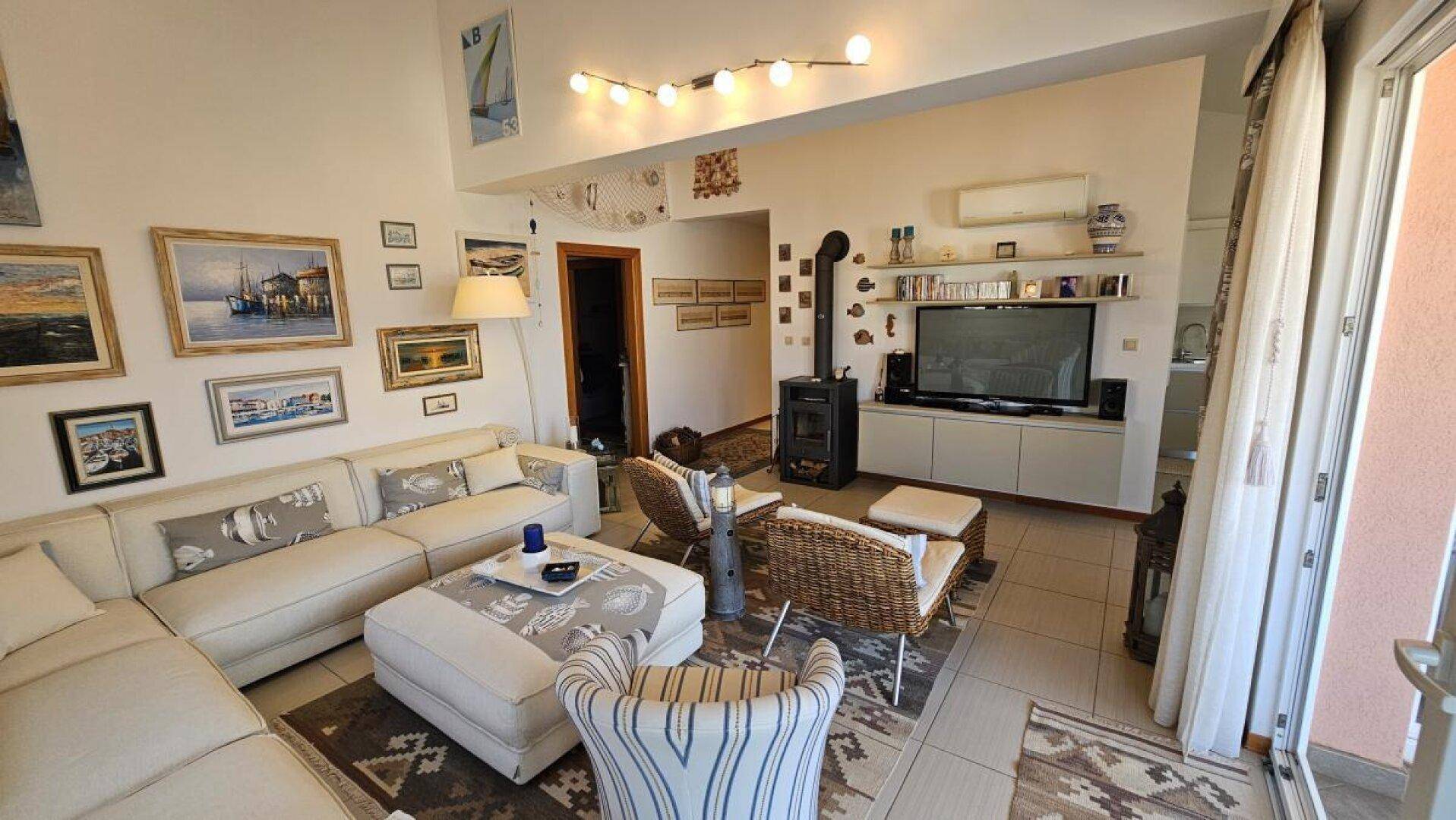 Gemütliches Wohnzimmer mit großem Sofa, Fernseher und einem Holzofen, mit Balkonzugang.