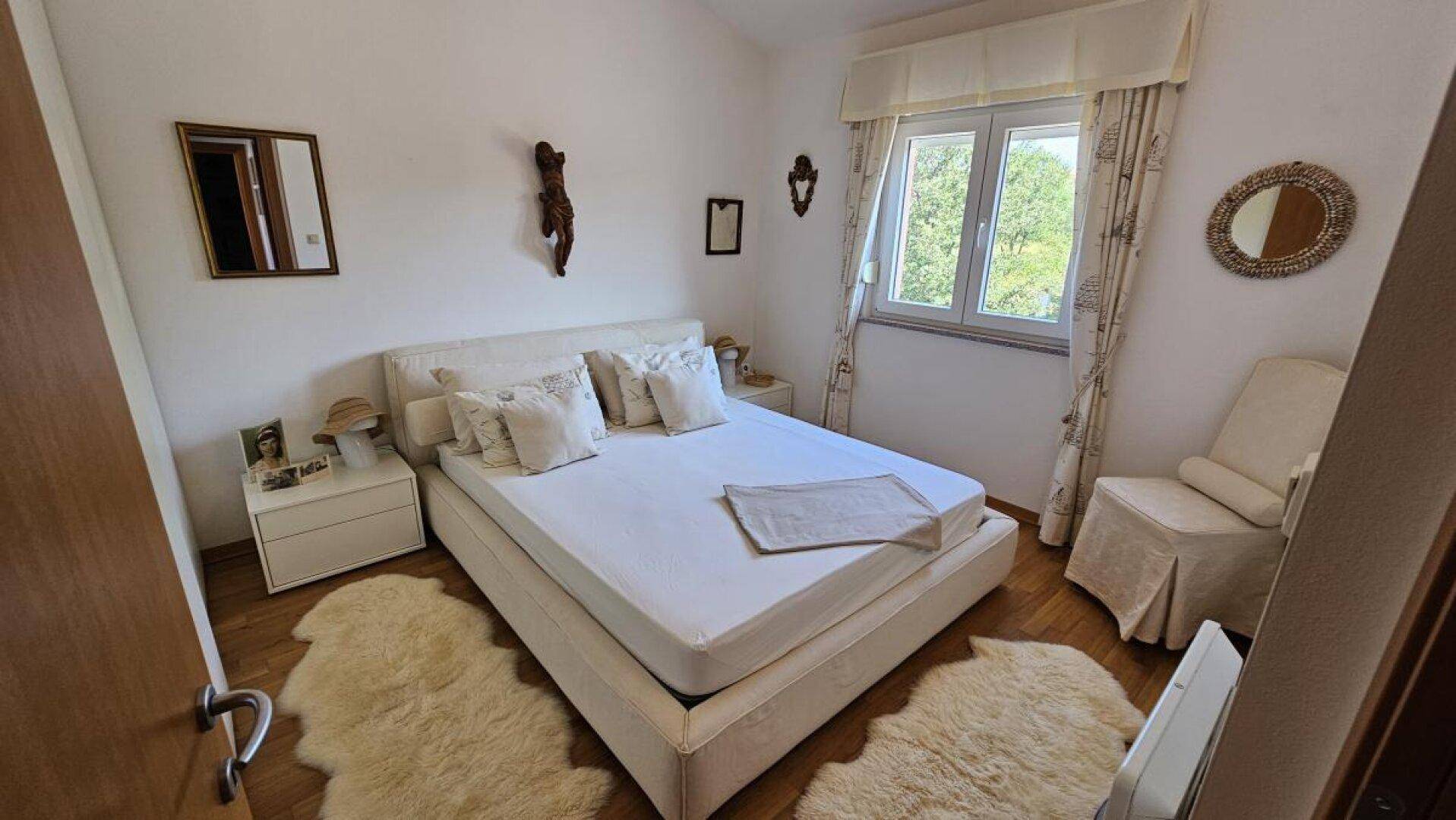 Helles Schlafzimmer mit Doppelbett, Nachttischen und Fenster, ausgestattet mit Holzfußboden.