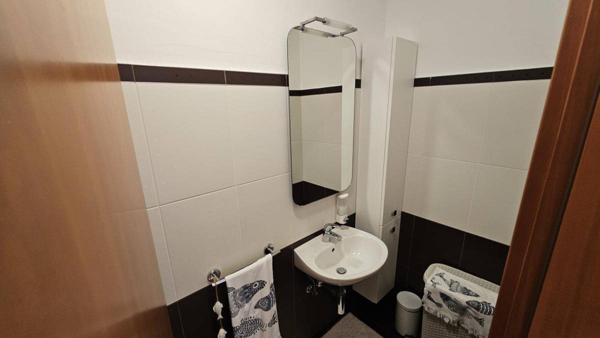 Kleines Gäste-WC mit Waschbecken, Spiegel und zweifarbigen Fliesen an den Wänden.