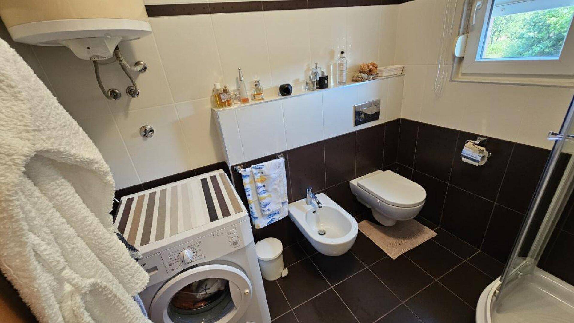 Badezimmer mit WC, Bidet, Waschmaschine und Warmwasserbereiter, funktional eingerichtet.