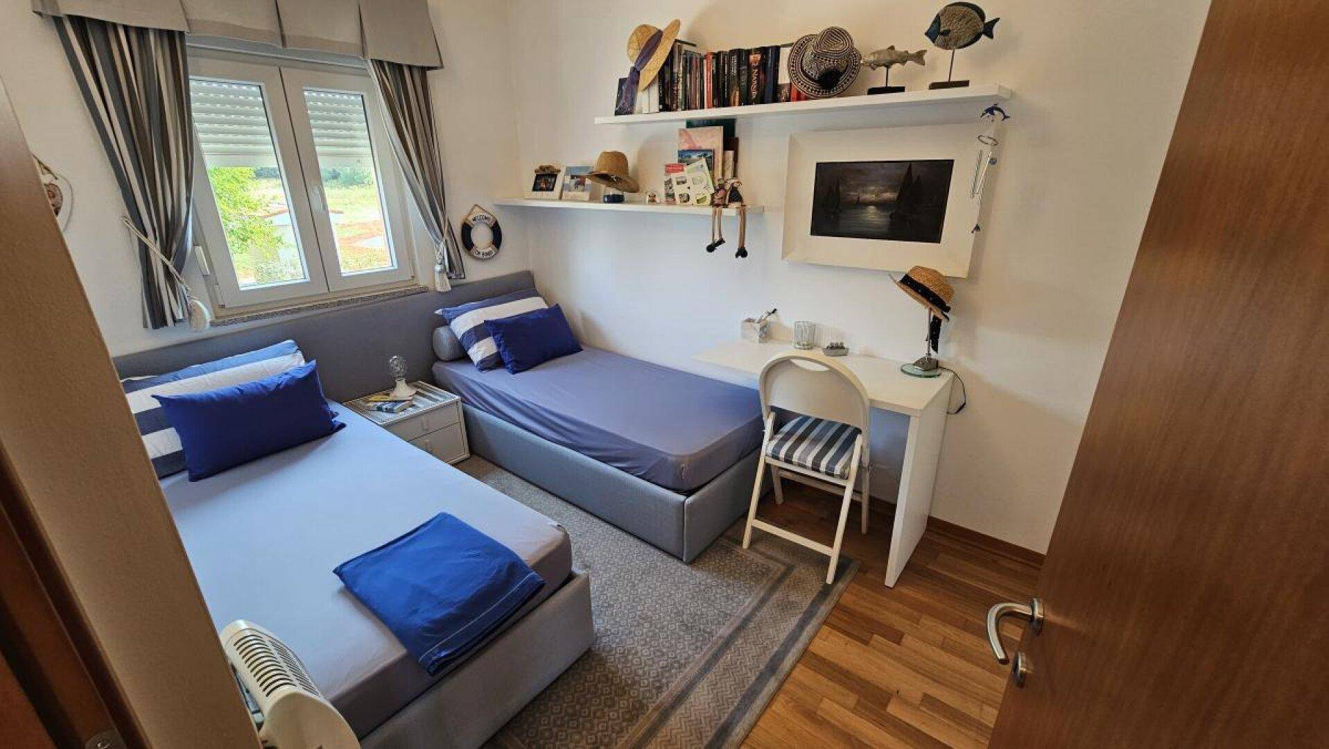 Kinderzimmer mit zwei Einzelbetten, Schreibtisch und Fenster, ausgestattet mit Holzfußboden.