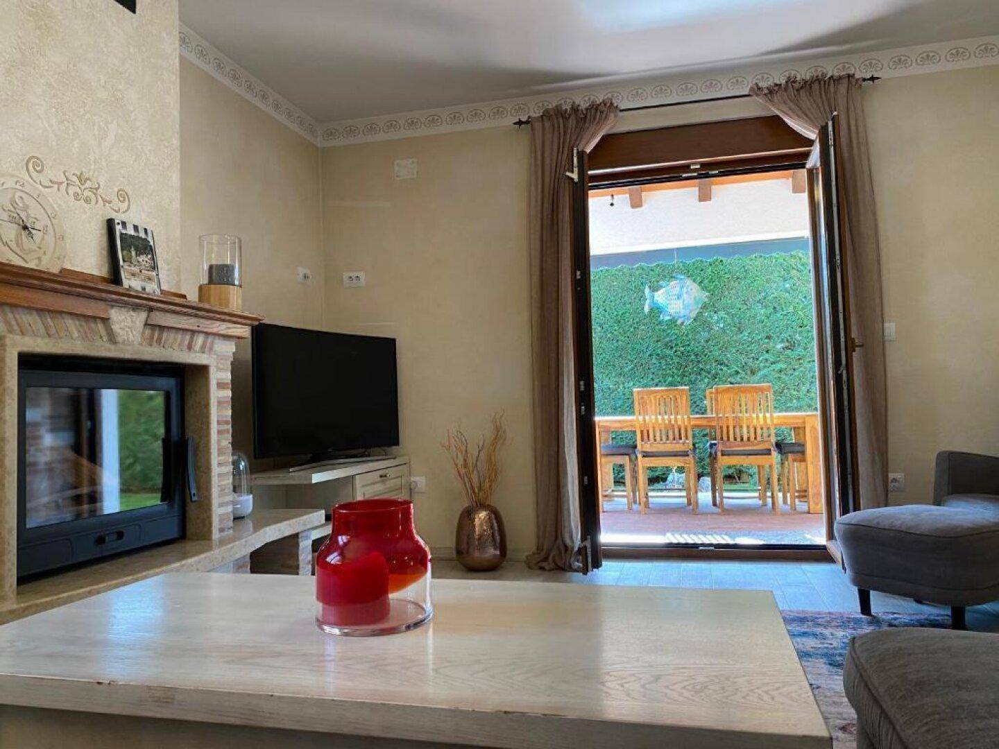 Wohnzimmer mit Kamin, Fernseher und Zugang zu einer überdachten Außenterrasse.