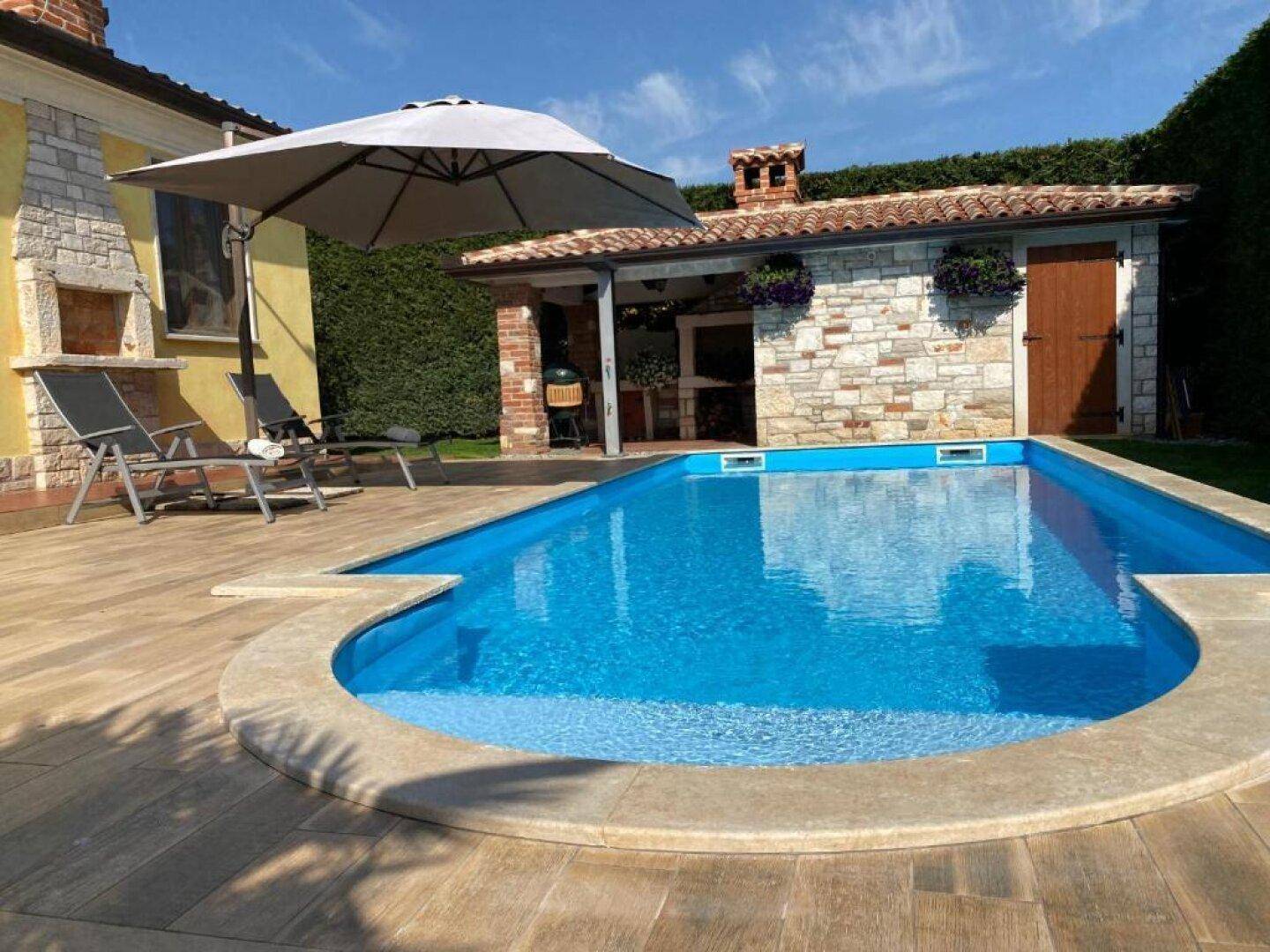 Außenbereich mit Pool, gepflasterter Terrasse und einem kleinen Gebäude mit Steinverkleidung.