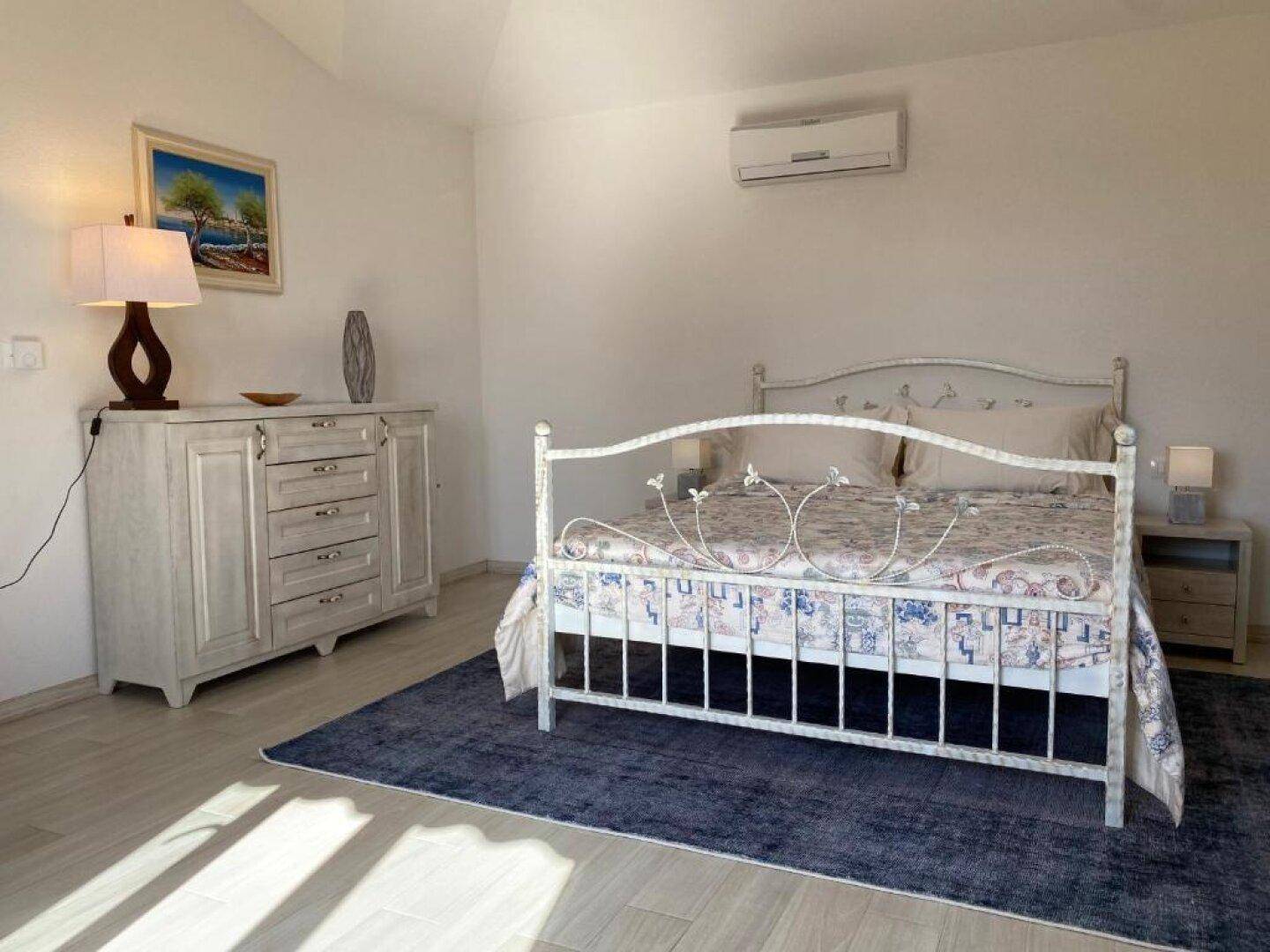 Helles Schlafzimmer mit Doppelbett, Kommode, Klimaanlage und viel Tageslicht.