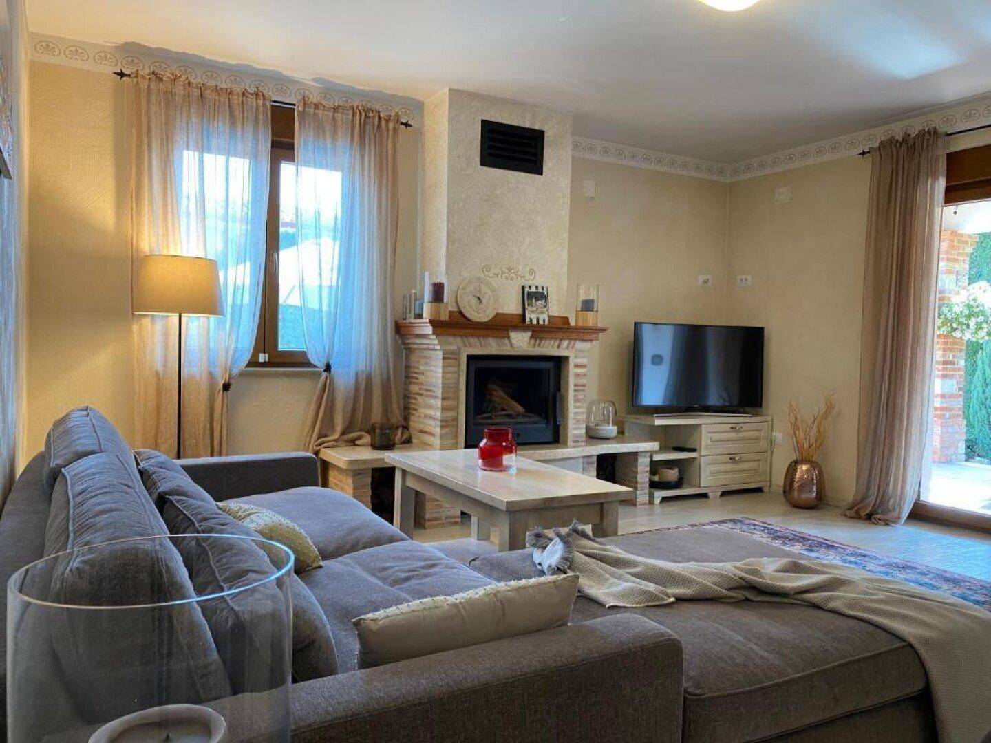 Gemütliches Wohnzimmer mit großem Sofa, Kamin und Vorhängen an den Fenstern.