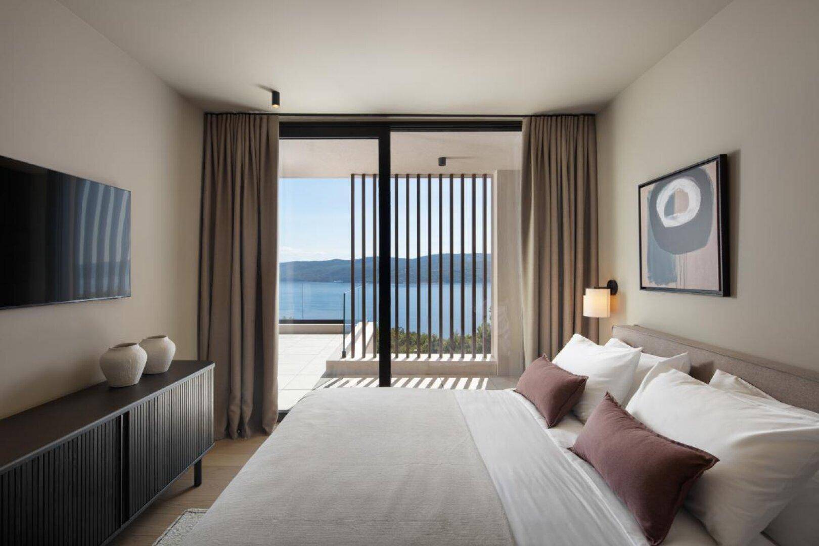 Helles Schlafzimmer mit Doppelbett und Zugang zu einem Balkon mit Meerblick.