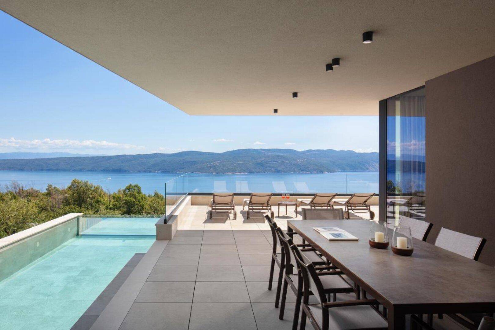 Große Sonnenterrasse mit Liegestühlen und Esstisch, direkt am Infinity-Pool mit Meerblick.