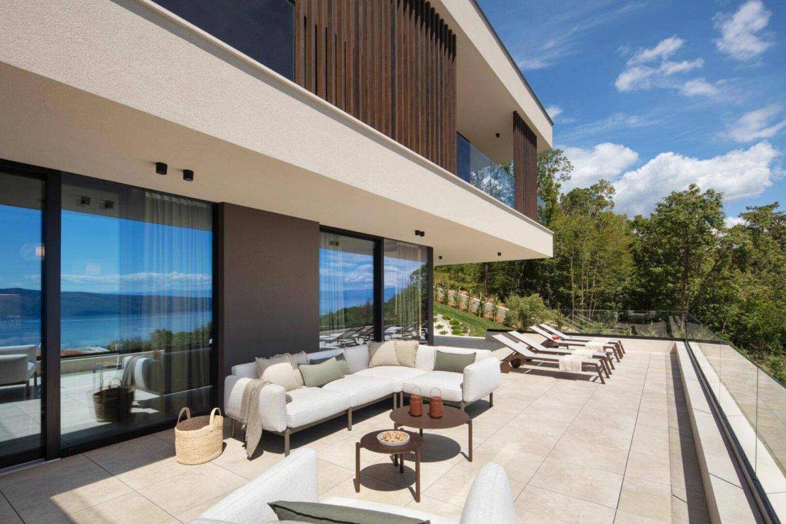 Geräumige Terrasse mit bequemen Loungemöbeln und Blick auf die grüne Umgebung und das Meer.