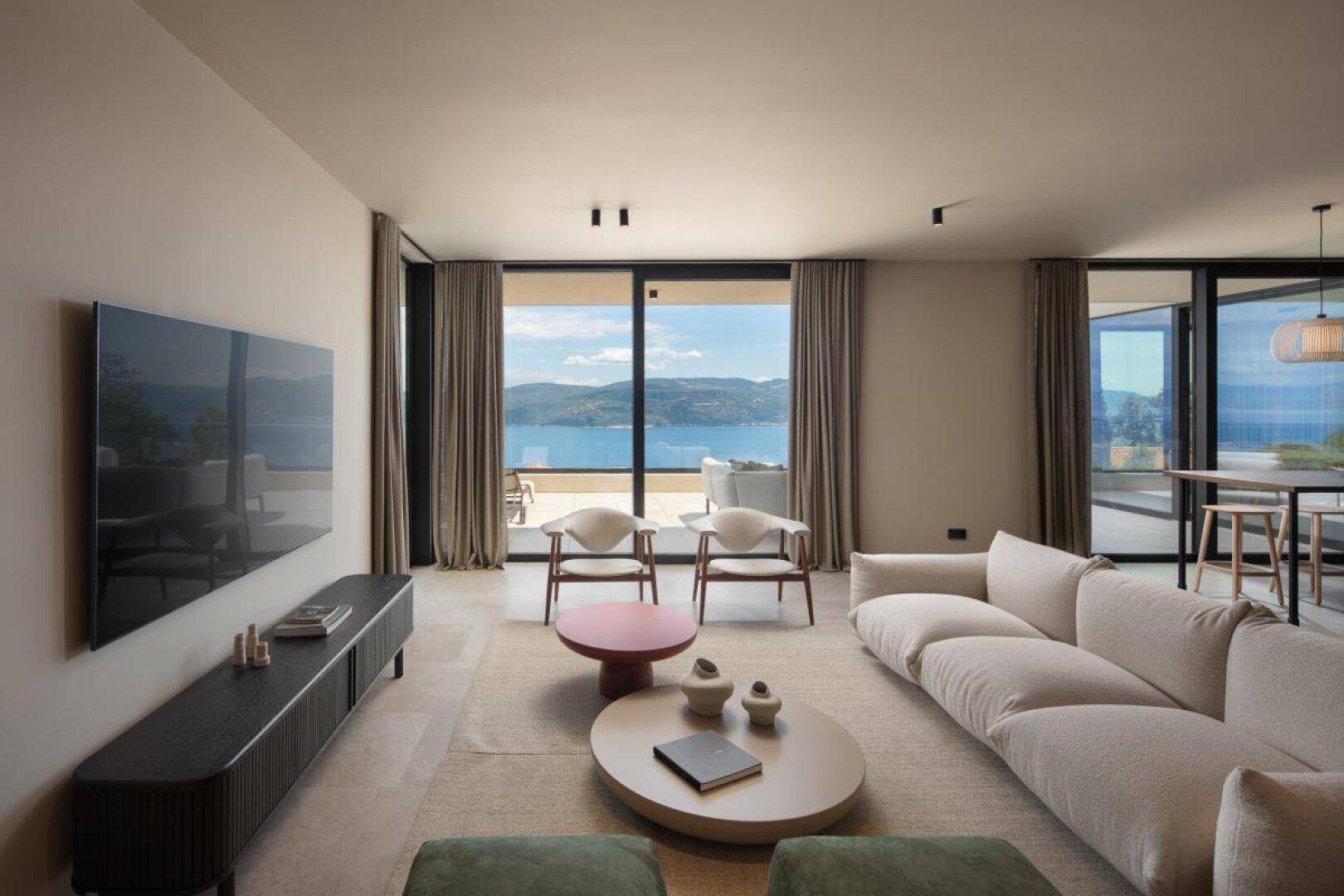 Helles Wohnzimmer mit bequemen Sofas, großem Fernseher und weitem Meerblick durch Panoramafenster.